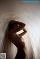 A naked woman standing in front of a white curtain.