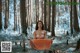 A naked woman sitting in the middle of a forest.