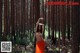 A naked woman in an orange skirt standing in the woods.