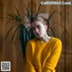 A woman in a yellow sweater leaning against a wooden wall.