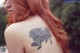 A woman with red hair and a tattoo on her back.