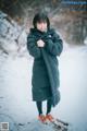 A young girl standing in the snow wearing a black coat.