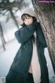 A woman leaning against a tree in the snow.