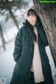 A woman leaning against a tree in the snow.