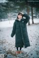 A woman standing in the snow wearing a black coat.