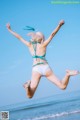 A woman in a bikini jumping in the air on the beach.