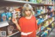 A woman in a red shirt standing in front of a shelf of snacks.