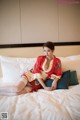 A woman in a red kimono sitting on a bed.