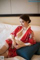 A woman in a red kimono sitting on a bed.