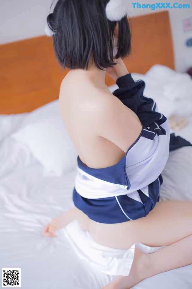 A woman in a blue and white outfit sitting on a bed.