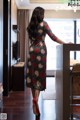 A woman in a floral dress and red high heels standing in a kitchen.