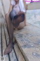 A woman in black pantyhose sitting on a wooden deck.