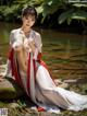 A woman in a white and red kimono sitting on a rock by a river.