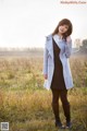 A woman standing in a field wearing a coat and boots.