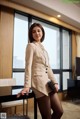 A woman in a beige suit standing next to a table.