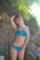 A woman in a blue bikini posing on a rock.
