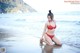 A woman in a red bikini sitting on the beach.