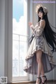 A woman with long black hair standing in front of a window.