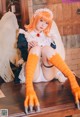 A woman in a white dress and orange gloves sitting on a table.