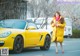 A woman in a yellow coat standing next to a yellow car.