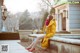 A woman in a yellow coat sitting on a stone wall.