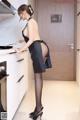 A woman in a black dress is standing in a kitchen.