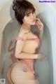 A woman in a pink lingerie sitting in a bathtub.