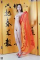 A naked asian woman standing in front of a yellow door.