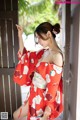 A woman in a red kimono leaning against a wooden door.