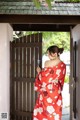 A woman in a red kimono standing in front of a wooden door.