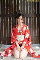 A woman in a red kimono sitting on the ground.