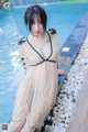 A woman in a long dress sitting by a swimming pool.